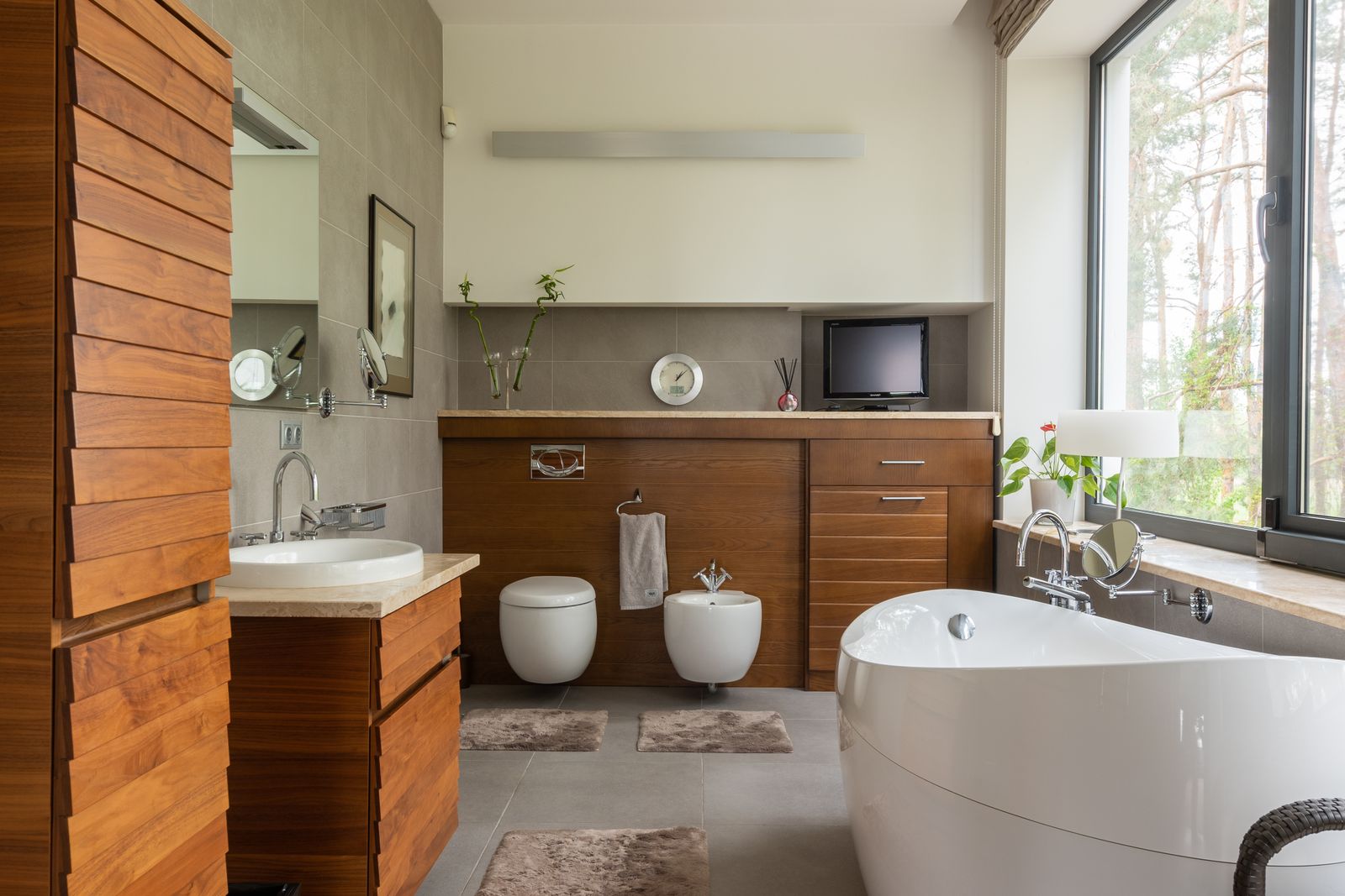 Freestanding tub, stone tile, and warm wood in a finished bathroom — stock detail photo